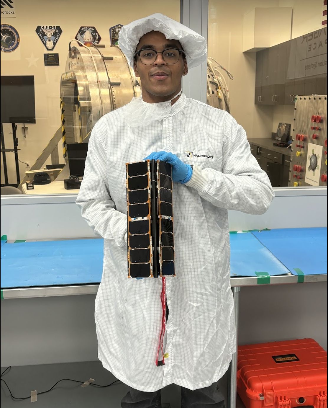 Sid Vaidyanathan in a cleanroom holding the DORA CubeSat.